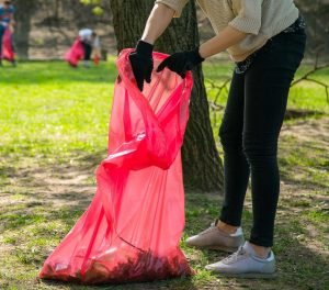 man and woman volunteer wearing picking up trash and plastic waste in public park. young people wearing gloves and putting litter into red plastic bags outdoors