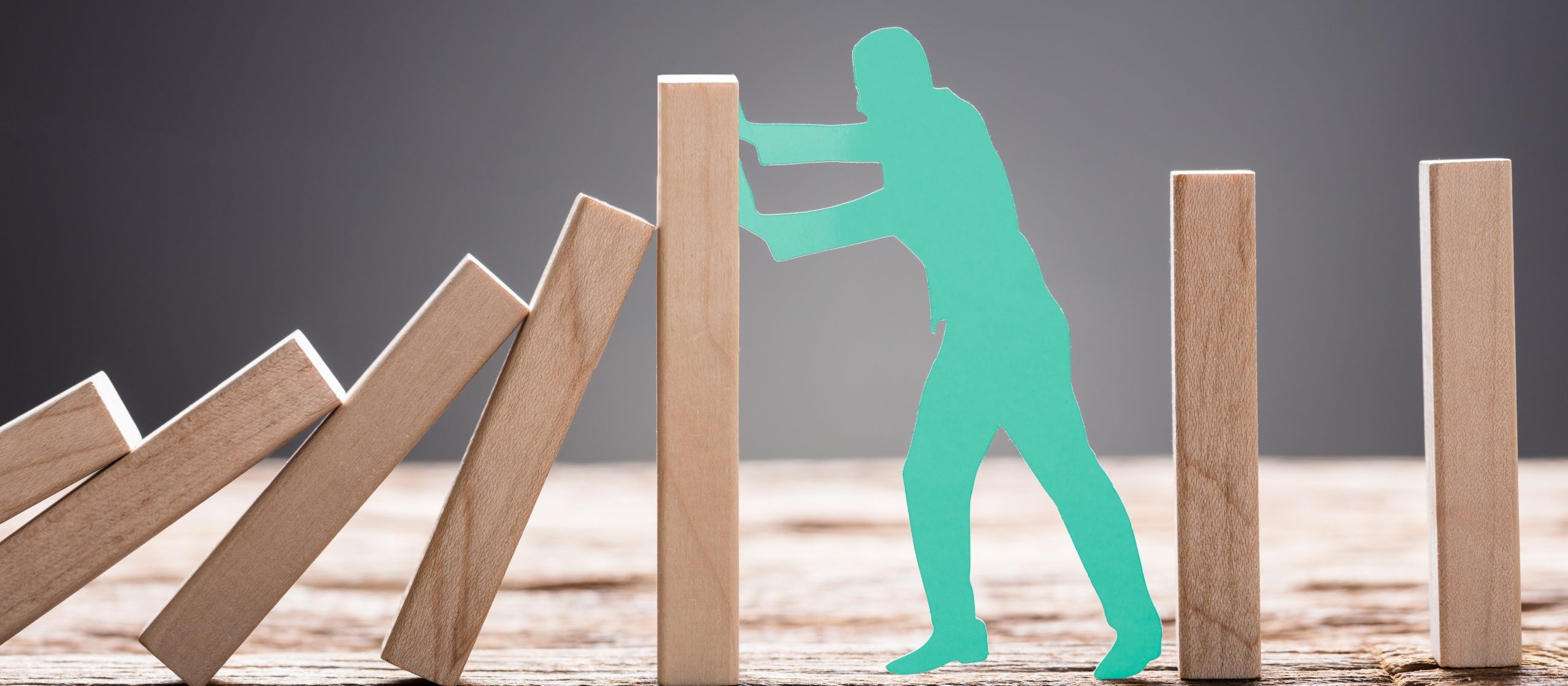 green paper man stopping wooden domino blocks